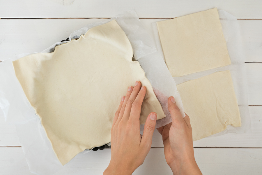 Das große Blätterteig-Quadrat mitsamt Backpapier in die Tarteform legen und leicht andrücken.